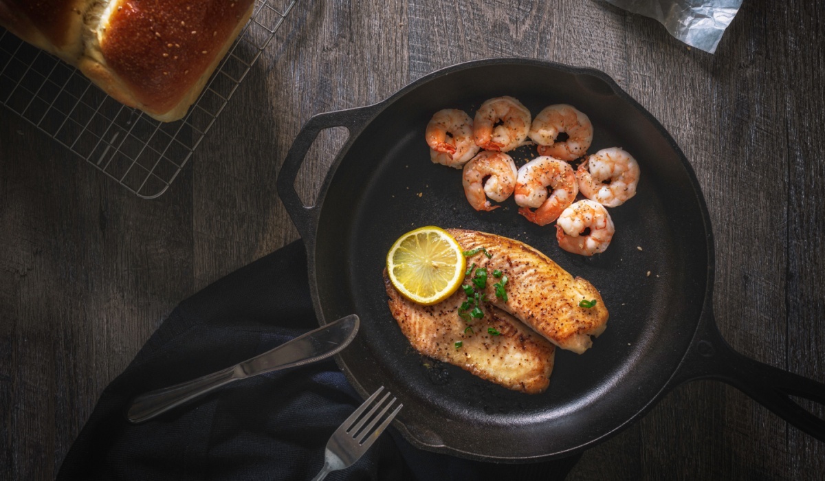 Fried fish shrimps in cast iron skillet and placed on wood table with bread and butter next to it.